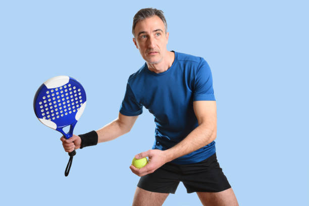 uomo che gioca padel in posizione di servizio con sfondo isolato blu - tennis men indoors serving foto e immagini stock