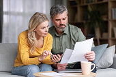 Married Middle Aged Couple Planning Budget Together, Reading Papers And Calculating Spents