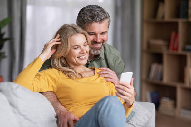 istock Happy middle aged couple using smartphone while relaxing on couch at home 1469858742