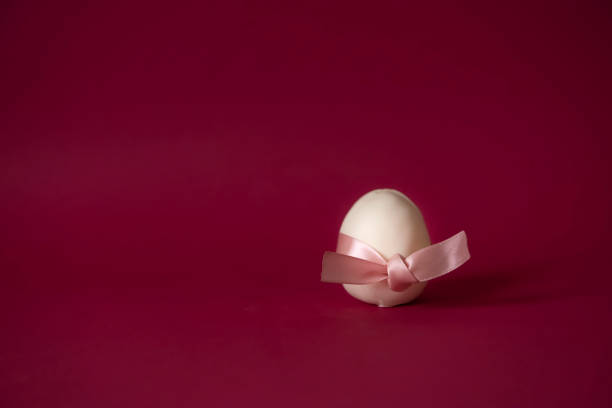 An egg-shaped cupcake covered with white chocolate, on a bright Viva Magenta background, tied with a pink satin ribbon. The concept of a female egg. Cake for parents for the birth of a girl.copy space