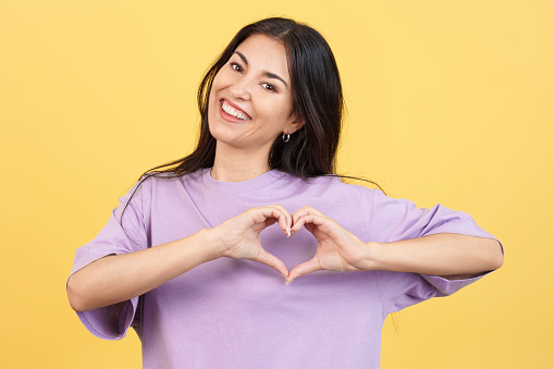 Woman representing a heart in the shape of fingers in studio with yellow background