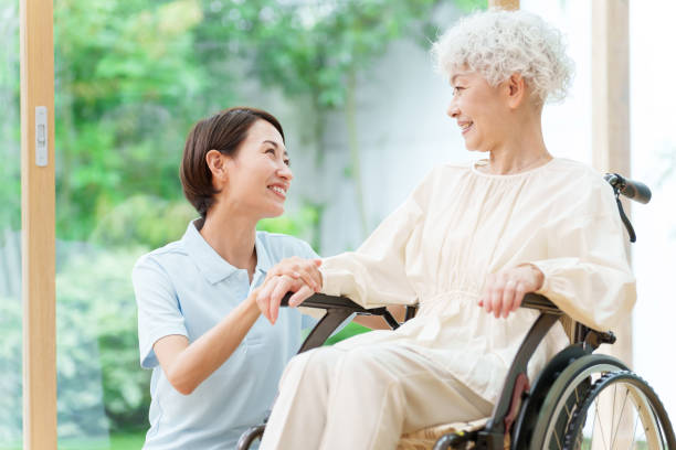 caregiver and senior woman riding wheelchair young asian caregiver and senior woman riding wheelchair sheltered housing stock pictures, royalty-free photos & images