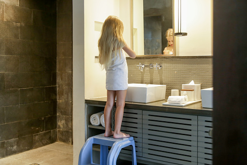 Portrait of toddler girl wrapped in towel in bathrom standing on children's step stool