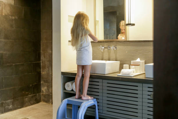 Portrait of toddler girl wrapped in towel in bathrom standing on children's step stool stock photo