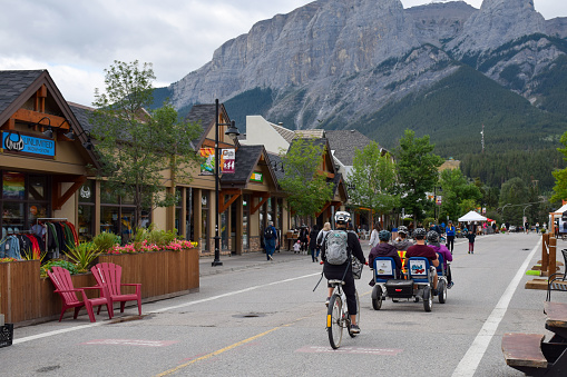 August 23, 2021 - Canmore, Alberta, Canada: Tourists riding bicycles on a street of Canmore in front of a mountain in Banff