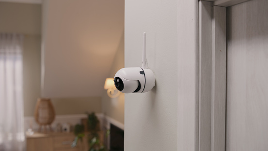 Close up shot of installed security camera on wall in modern apartment. CCTV camera with microphone and green indicator. Concept of monitoring system, surveillance and personal privacy.