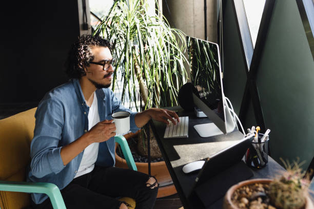 istock Young Hispanic Man Working from Home on Desktop Computer in Sunny Stylish Loft Apartment. Creative Designer home office in Mexico Latin America 1469896780
