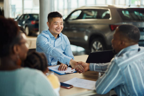 Happy Chinese car salesperson came to an agreement with his customers in a showroom. Happy Asian car salesman came to a successful agreement with black family during a meeting in a showroom. car salesperson stock pictures, royalty-free photos & images