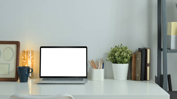 istock Home office desk with laptop, picture frame and potted plant on white table. Empty screen for text information or content. 1469899936