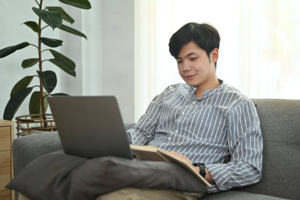 istock Pleasant young asian man surfing internet, checking email on laptop while sitting in cozy living room. 1469900006