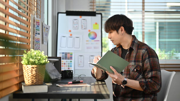 istock Side view of creative asian male working on mobile application software design project at modern modern home office. 1469900030
