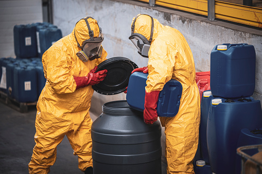Chemical plant workers in hazmat suit mixing chemicals and manufacturing acids for heavy industry.