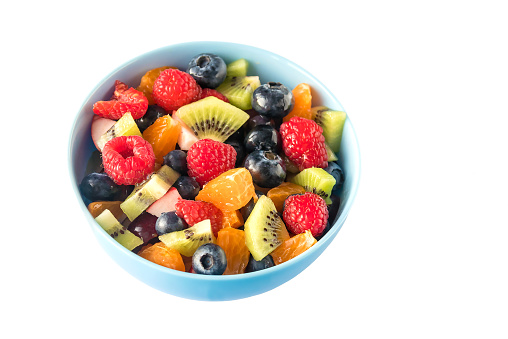 In a ceramic blue bowl, fresh healthy tasty fruit sliced salad for breakfast. Isolated on white background.