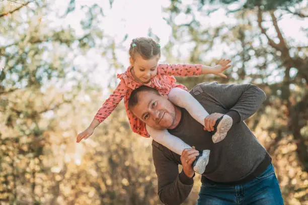 Photo of Happy Father And Child Having Fun Playing Outdoors. Smiling Young Dad And Daughter Spending Time Together In Nature. Parent And His Kid Relaxing In Park.