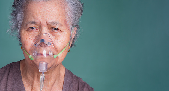 Close-up of an elderly Asian woman wearing a medical breathing mask. Sick senior woman wearing an oxygen mask inhalation, pneumonia coronavirus pandemic and undergoing treatment.