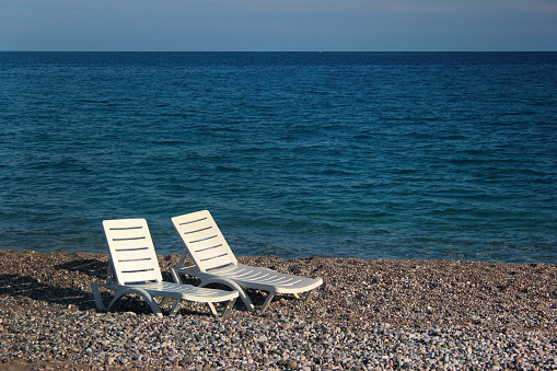 Two wooden Adirondack chairs rest on rocky Town Neck Beach in Sandwich, Massachusetts near the entrance of the Cape Cod Canal.