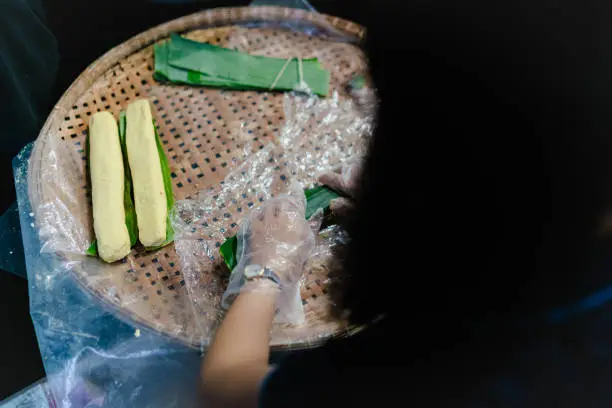 Making (wrapping) Tet Cake (Bánh Tét), the Vietnamese lunar new year Tet food outdoor with old woman hands and ingredients. Closed-up.