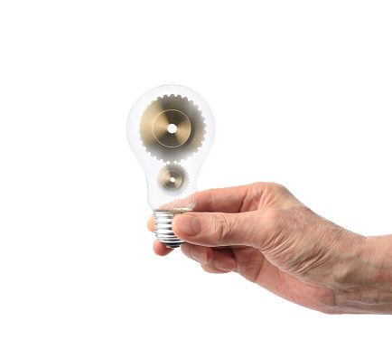 Close-up of hand holding a light bulb with gears against white background.