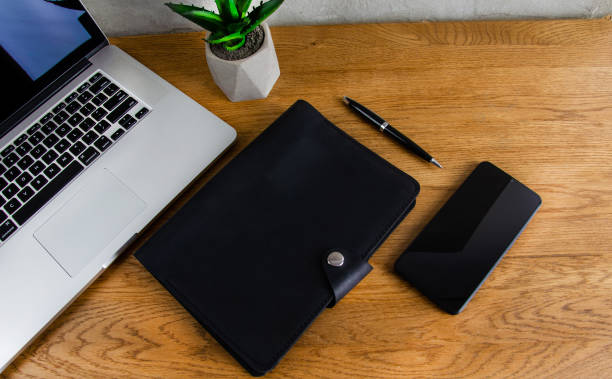 leather notepad on a wooden table. Phone, laptop and notebook on the table. Concrete wall on the background. Lifestyle.