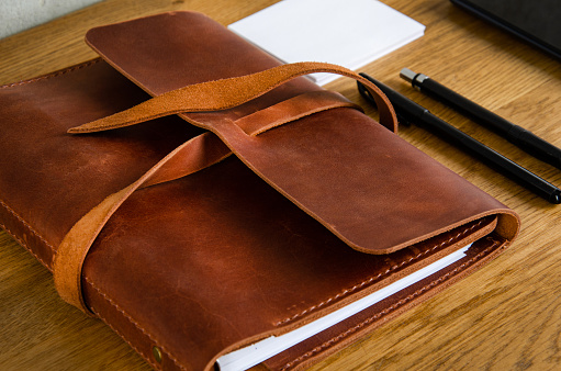 leather notepad on a wooden table. Phone, laptop and notebook on the table. Concrete wall on the background. Lifestyle.
