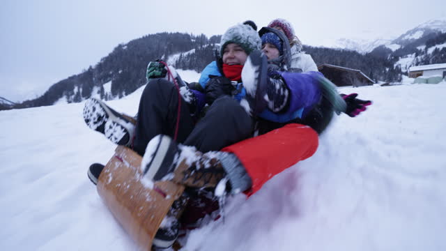 Three teenage kids sledding on hill on a winter day