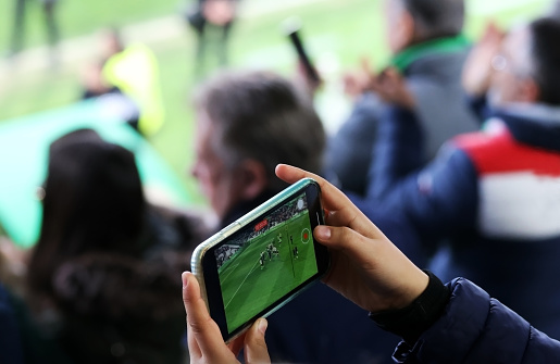 A fan recording a football match from the stands with his mobile phone. Selective focus.