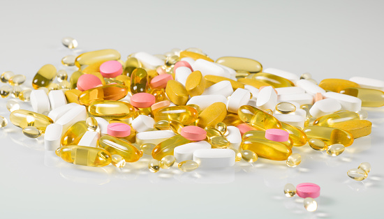 Heap of multicolored pills and capsules with bioadditives with reflection on glass background.