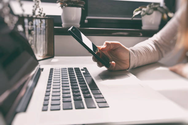 istock The woman is using the mobile phone while working on laptop 1469912344