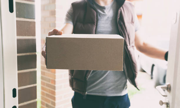 Deliveryman gives the carton box to the customer at the door of his house stock photo
