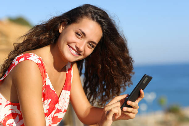 Tourist on the beach looks at camera holding phone stock photo