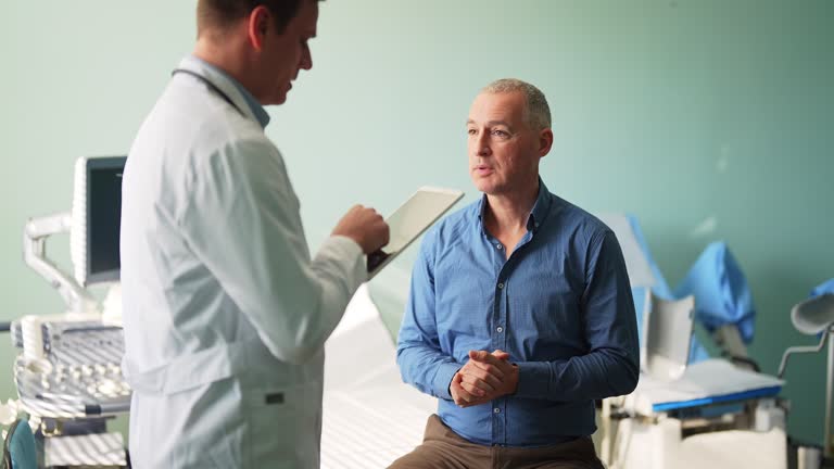 Male doctor consulting mature man, holding tablet and prescribing treatment to his patient