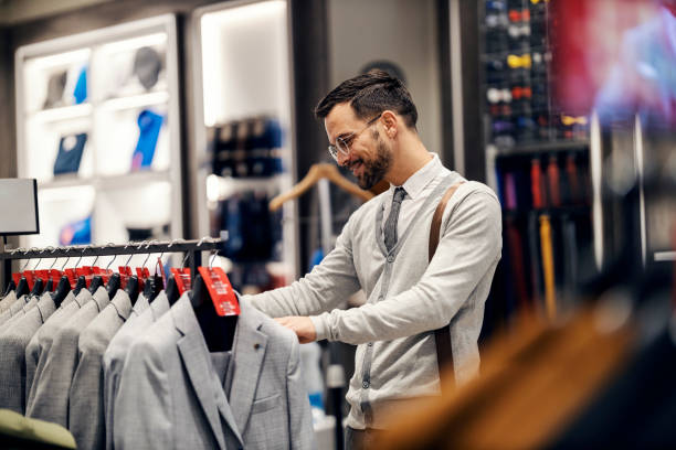 A young happy man in smart casual is choosing suit in boutique. stock photo