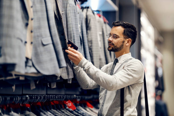 istock A young elegant man is standing at clothing store and looking for proper suit. 1469916094