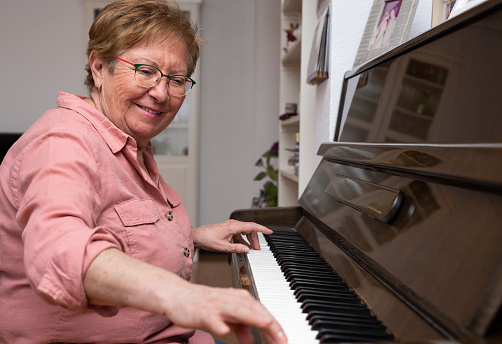 Smiling senior woman playing the piano at home.