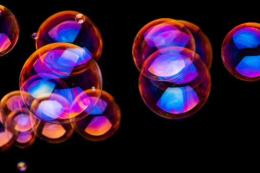 Metallic glowing colorful soap bubbles in the air in front of a blurry abstract background
