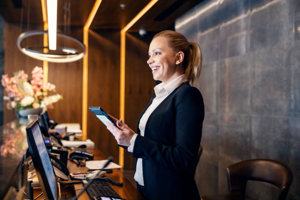 A happy receptionist is talking with hotel guest and making a reservation on a tablet. stock photo