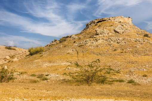 Untapped limestone quarry with golden grass and arid landscape, sky with clouds, Sindh, Pakistan