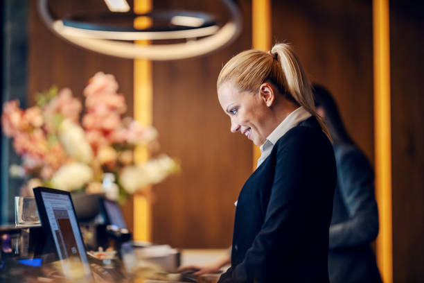 una recepcionista está haciendo una reserva en línea en la recepción de un hotel. - hotel reception fotografías e imágenes de stock