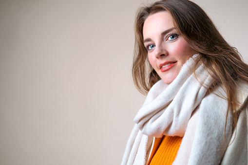 Studio shot of a woman in a white scarf and orange sweater. Space for text on the side.