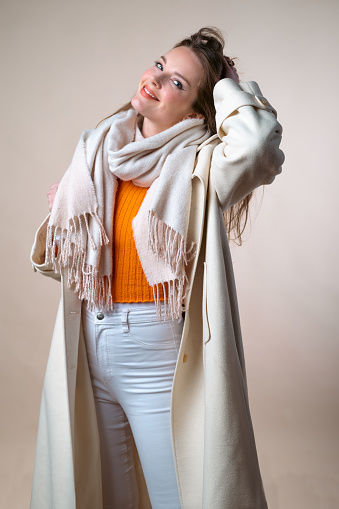 Studio shot of a woman in a white coat and orange sweater. Winter fashion.