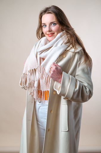 Studio shot of a woman in a white coat and orange sweater. Winter fashion.