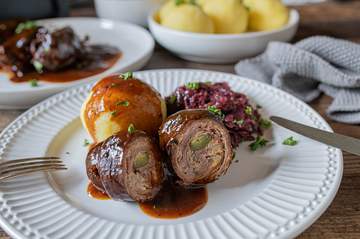 Traditional german beef roulades with mustard, bacon, onion, pickle filling. Served with red cabbage, potato dumplings and delicious brown gravy on a plate. Sunday or holiday meal