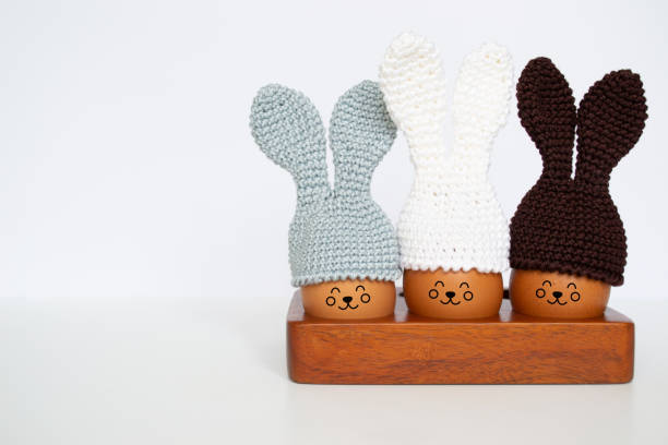 istock Knitted Easter eggs with bunny ears hats in a wooden stand on a white table. Soft focus. 1469922692