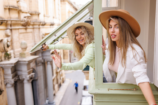 Young female tourists enjoying view from apartment window on their vacation