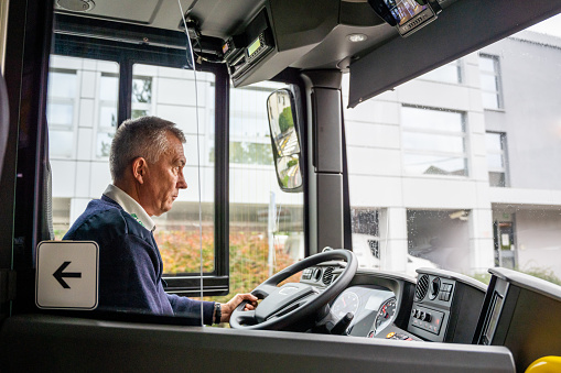Senior adult caucasian male bus driver sitting in public transport and holding steering wheel, side view
