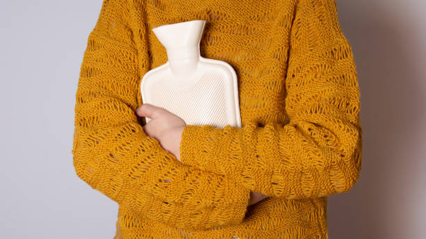 Hot water heating pad is winter essentials.  Power outages and difficulties with heating. Saving electricity. Woman in orange sweater holding heating pad.