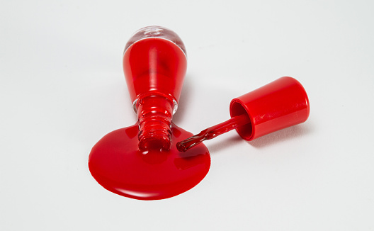 Red nail polish spilled from a glass bottle, composition on a white background.