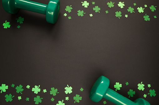 Two heavy green dumbbells and shamrock leaf clover. Healthy fitness lifestyle composition for St. Patrick's Day. Gym workout and training flat lay concept with copy space.
