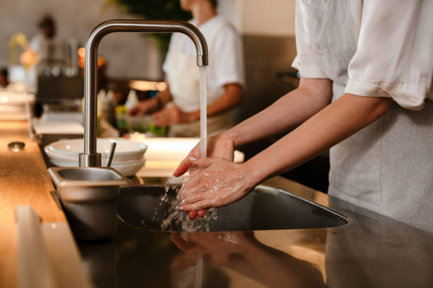 Young chef woman washing hands while working in restaurant kitchen stock photo
