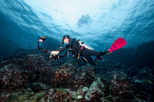 Male Scuba diver with camera diving over coral reef at Richelieu Rock, a famous scuba diving dive site and stunning underwater landscape in Thailand.